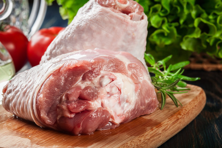 Raw turkey knuckle on wooden cutting board ready for baking.
